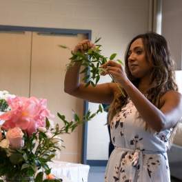 Woman arranging pink flowers and greenery at a table