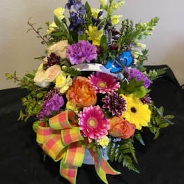 Colorful mixed flower arrangement in a white container with a plaid ribbon
