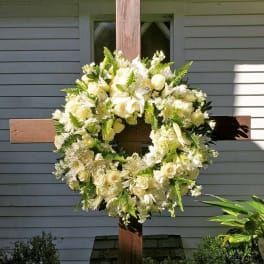 Large white floral wreath with roses and lilies on a wooden cross outdoors