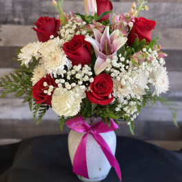Bouquet of red roses, pink lilies, and white daisies in a white vase with a pink ribbon
