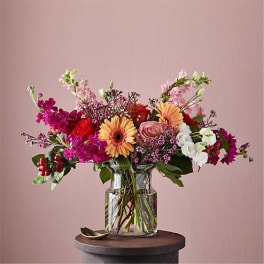 Colorful mixed bouquet with gerbera daisies, roses, and snapdragons in a clear glass vase.