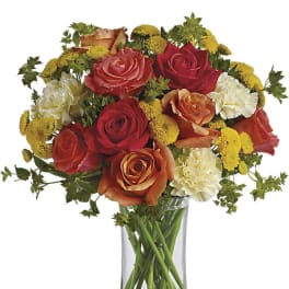Mixed roses and yellow button flowers in a clear glass vase