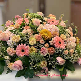 Low casket-style spray of pink and peach roses, gerberas, carnations, and mums with white filler flowers