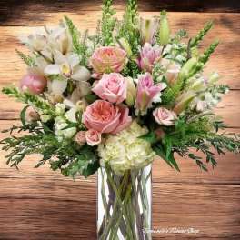 Tall arrangement of pink roses, lilies, orchids, and white hydrangeas in a clear glass vase