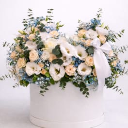 Low arrangement of white and peach flowers with blue accents in a round white hat box with ribbon
