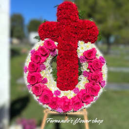 Standing funeral wreath of pink roses and white mums with a red carnation cross on an easel