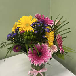 Tall vase arrangement of pink gerbera daisies, yellow gerbera daisies, purple asters, and pink roses.