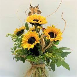 Tall arrangement of yellow sunflowers with rustic accents in a clear glass vase