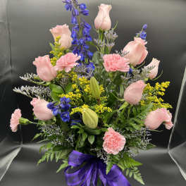 Tall mixed bouquet of pink roses and carnations with blue delphinium in a green vase with purple bow