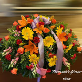 Large round spray of orange lilies, yellow gerberas, roses, and red carnations with a lavender bow.