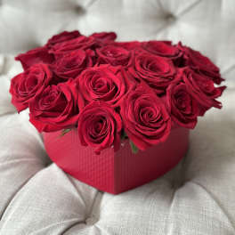 Red roses arranged in a pink heart-shaped box