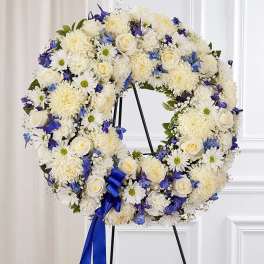 Standing wreath of white roses, chrysanthemums, and daisies with blue flowers and ribbon