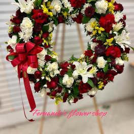 Standing wreath of red and white roses with white lilies, mums, and a red bow on an easel.