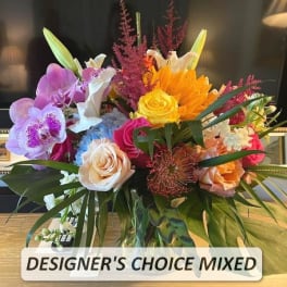 Mixed arrangement of orchids, roses, lilies, hydrangea, and sunflowers in a clear glass vase