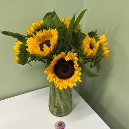 Vase arrangement of yellow sunflowers with dark centers in a clear glass vase on a white table