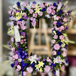 Standing rectangular wreath of pink, purple, yellow, and white flowers with ribbons on an easel