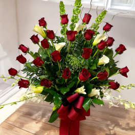 Tall arrangement of red roses, white calla lilies, and green bells of Ireland with a red bow.