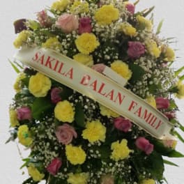 Standing floral wreath with pink and yellow roses and a condolence ribbon