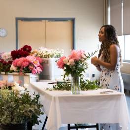 Woman arranging pink and white flowers at a table with buckets of blooms