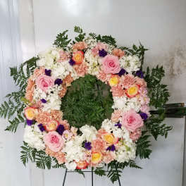 Circular floral wreath on a black stand with pink, white, and peach flowers