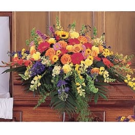 Bright mixed casket spray of yellow, orange, and pink flowers on a wooden casket