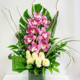 Pink orchids and white roses arranged in a tall green vase
