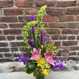 Tall mixed bouquet in a glass vase with pink lilies and purple flowers