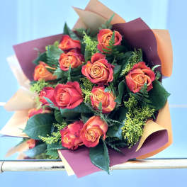 Bouquet of orange and red roses wrapped in peach and burgundy paper against a light blue background
