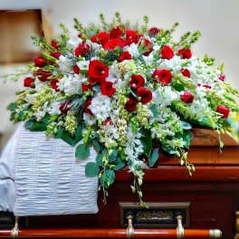 Red and white casket spray of roses and mixed white flowers on a wooden casket