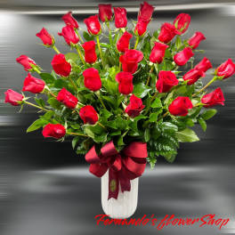 Tall white vase filled with many red roses and foliage, finished with a large red satin bow