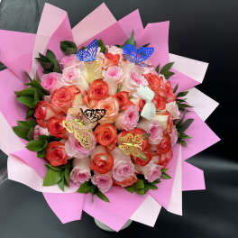Round bouquet of pink and coral roses with butterfly accents wrapped in pink paper
