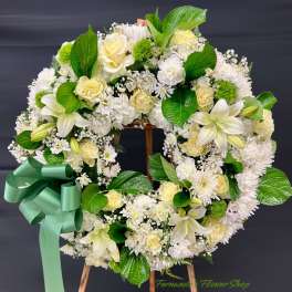Standing wreath of white and pale yellow roses, lilies, and mums with a large green ribbon bow on an easel
