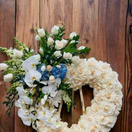 Heart-shaped ivory rose wreath with white orchids and blue hydrangeas on a wooden easel.