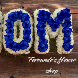 Floral letters spelling MOM with blue roses on white flowers against wood background
