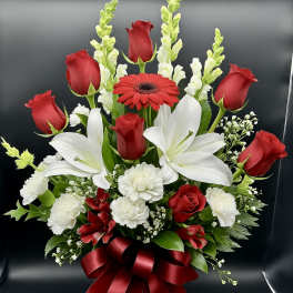 Tall arrangement of red roses, white lilies, and carnations in a glass vase with a red bow