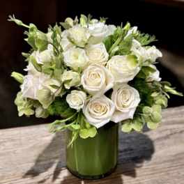 Compact arrangement of white roses and green blooms in a green glass cylinder vase