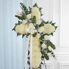 Standing cross-shaped spray of white flowers with white roses and ribbon on an easel.