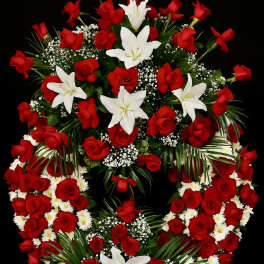 Standing wreath of red roses, white lilies, and small white blooms with decorative greenery in a double-ring design