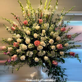Large fan-shaped arrangement of white and pink roses with tall white blooms in a white pedestal vase