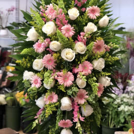 Tall standing spray with white roses and pink gerbera daisies on a green foliage backdrop.