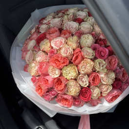 Large round bouquet of cream, peach, and pink roses wrapped in white paper with pink ribbons.