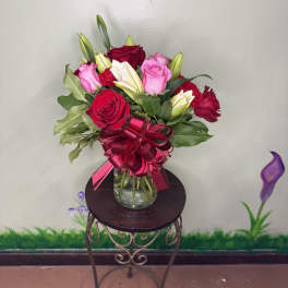 Mixed bouquet of red and pink roses with white lilies in a clear glass vase with a red bow.