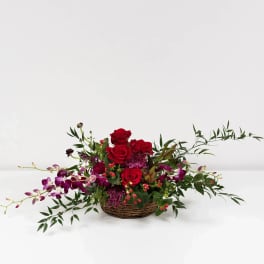Basket arrangement of red roses and purple orchids