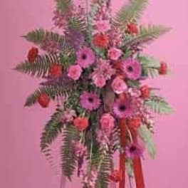 Tall pink and red standing flower spray with ferns on an easel against a pink background.