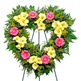 Heart-shaped standing wreath with yellow lilies and pink gerbera daisies on a metal easel.