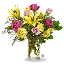 Tall arrangement of yellow lilies, yellow carnations, and lavender roses in a clear glass vase