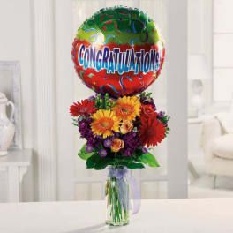 Tall mixed bouquet in a clear vase topped with a colorful Congratulations balloon