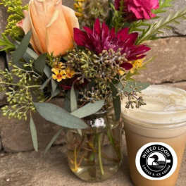 Bouquet of peach and magenta flowers in a glass vase beside a lidded iced drink