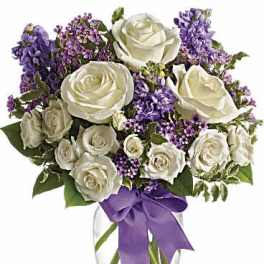 White roses and purple flowers in a clear glass vase with a purple ribbon