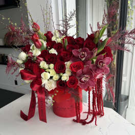 Large red and white rose arrangement with mauve orchids in a red hatbox with cascading red accents.